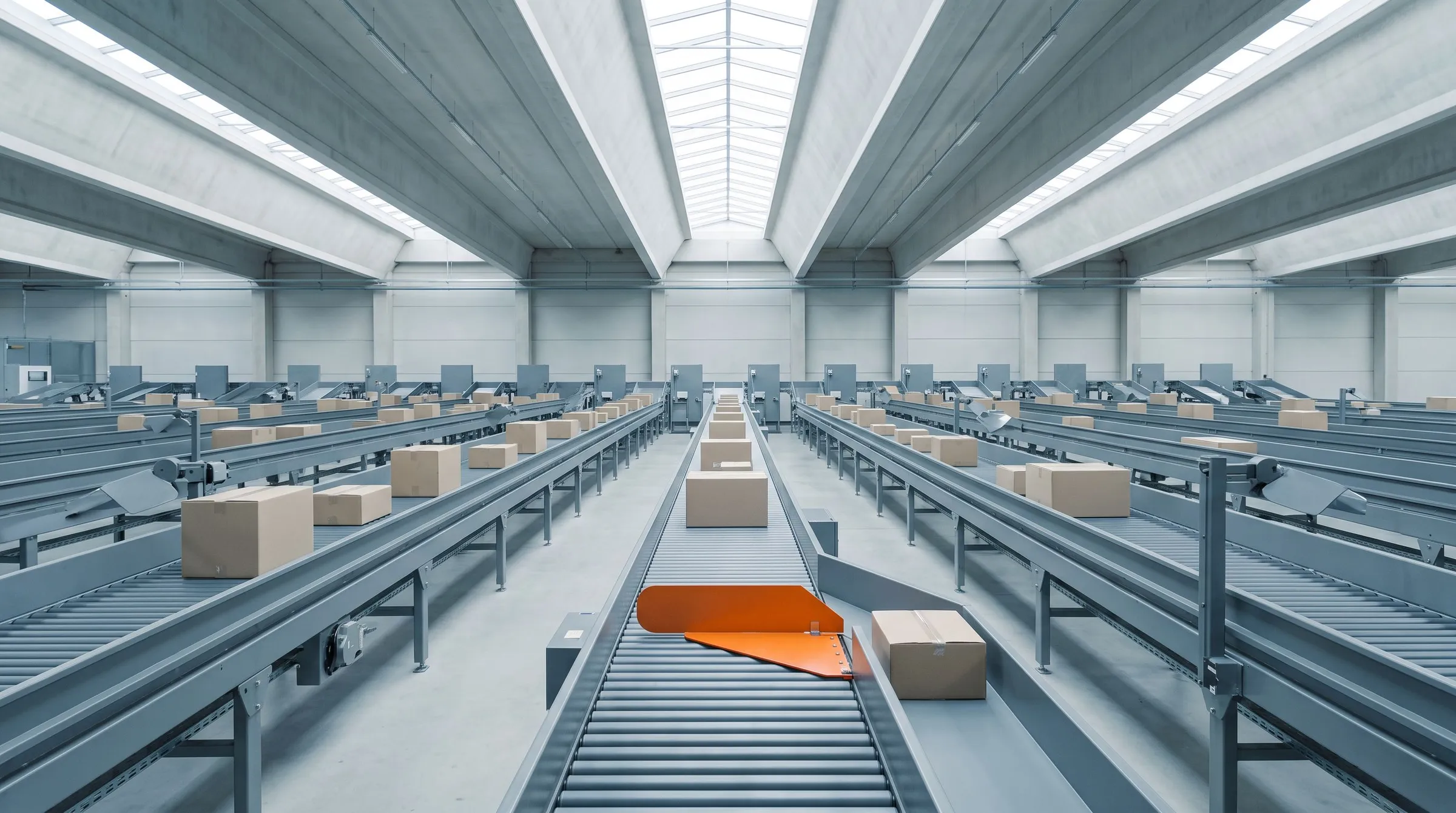 A quiet parcel sorting hall with long grey conveyors of plain boxes and a single orange diverter paddle steering one box toward a side lane