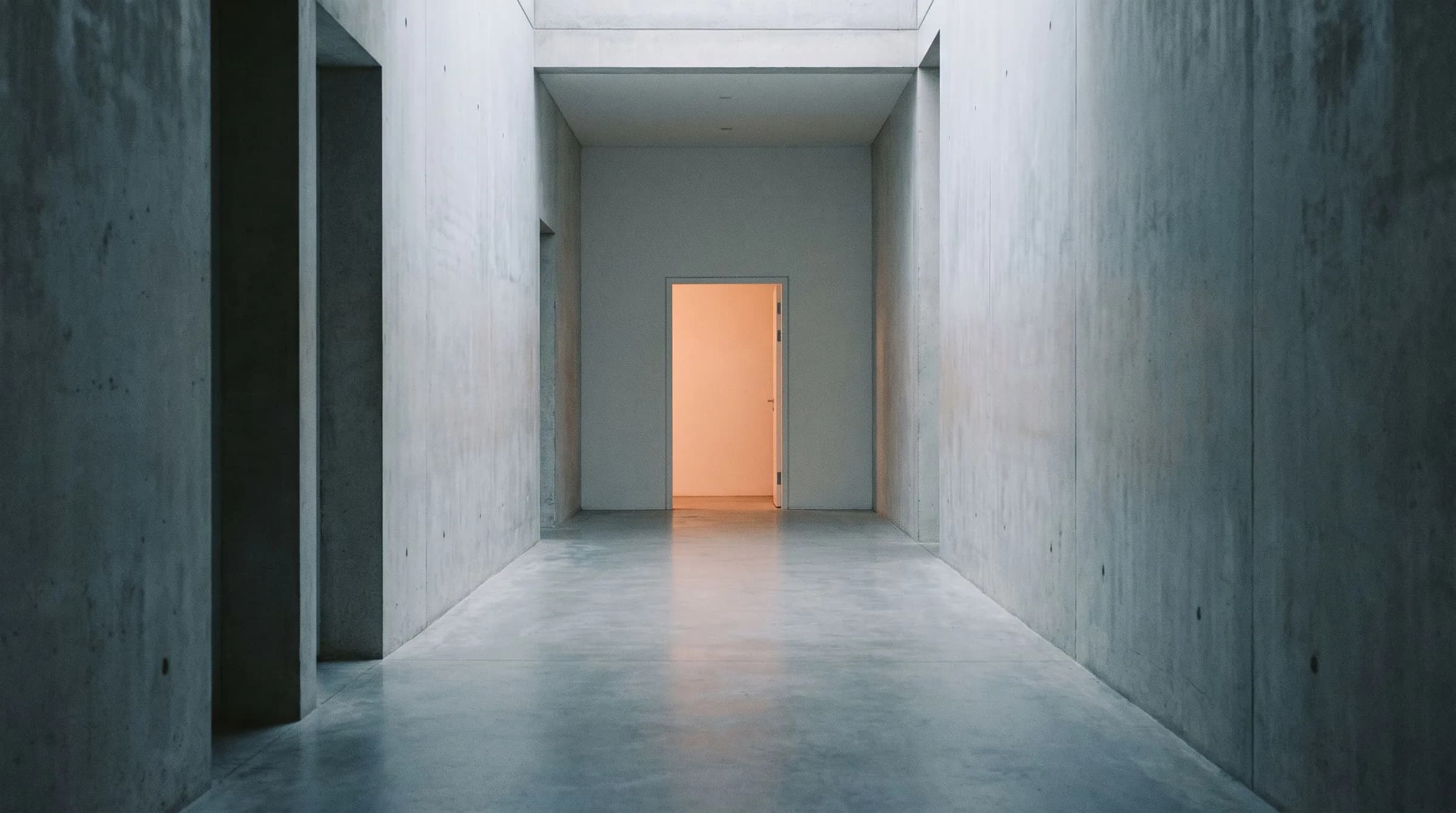 A long fog-grey corridor leading to a single doorway glowing orange at the far end