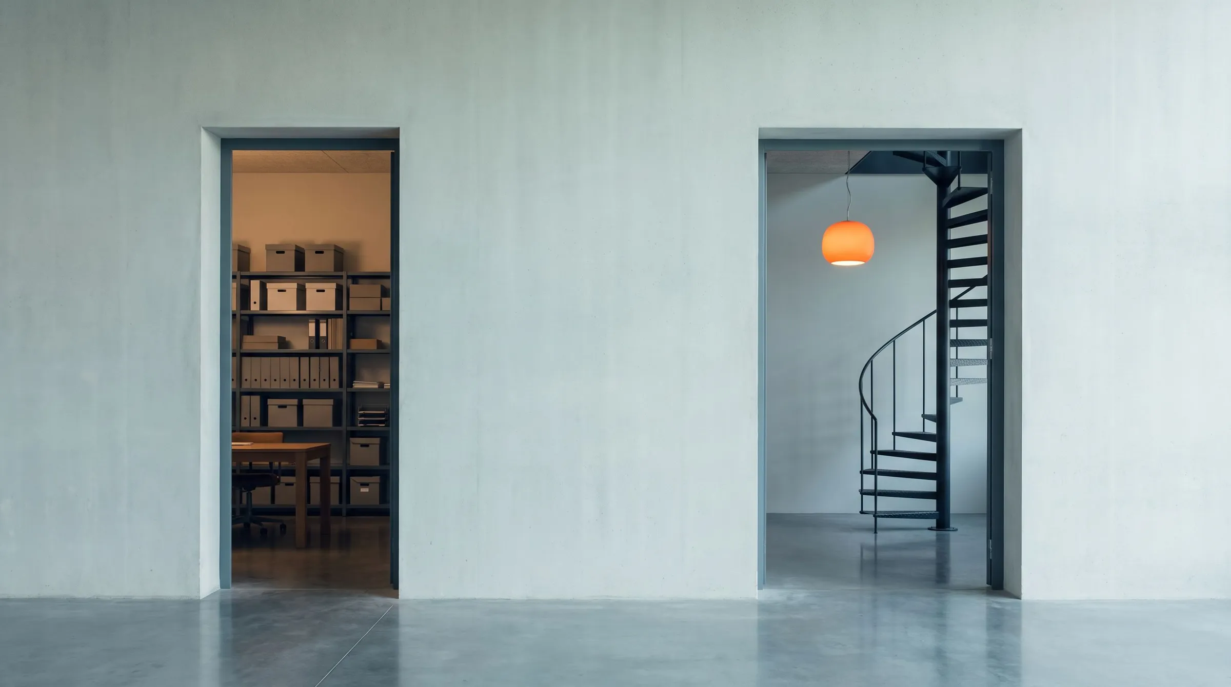 Two doorways in a pale concrete wall, one opening onto shelves of grey boxes, the other onto a spiral staircase under an orange pendant light