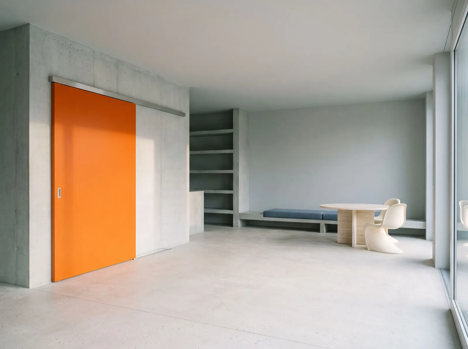 A calm concrete interior with one orange sliding door fitted into the existing wall as if it had always been there